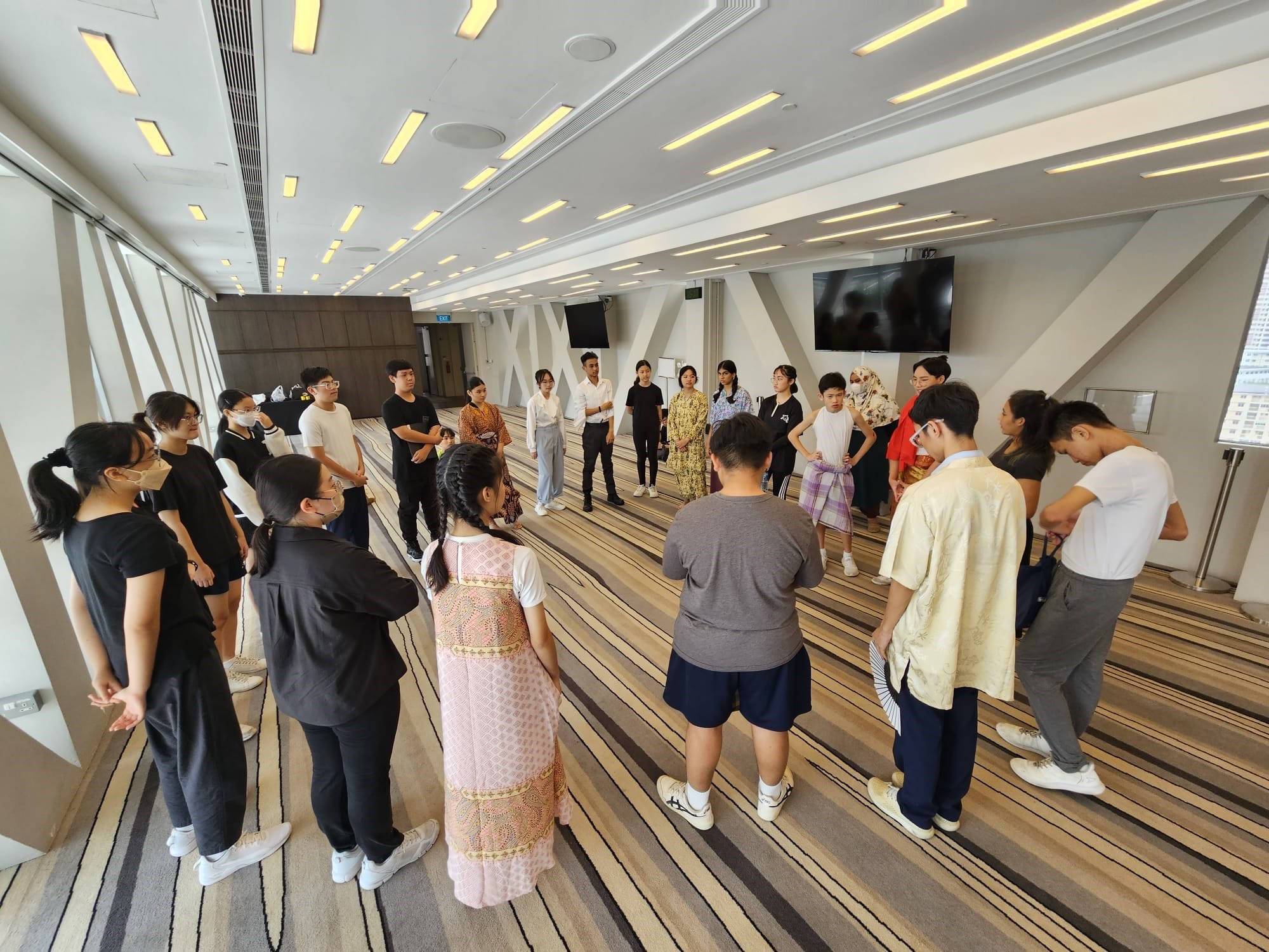 NV Drama members standing in a circle in a modern indoor hall with striped carpet.